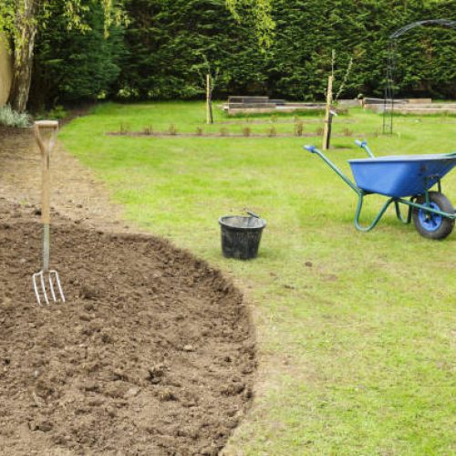 Preparing a freshly dug flower bed for planting in a garden with fork and wheelbarrow